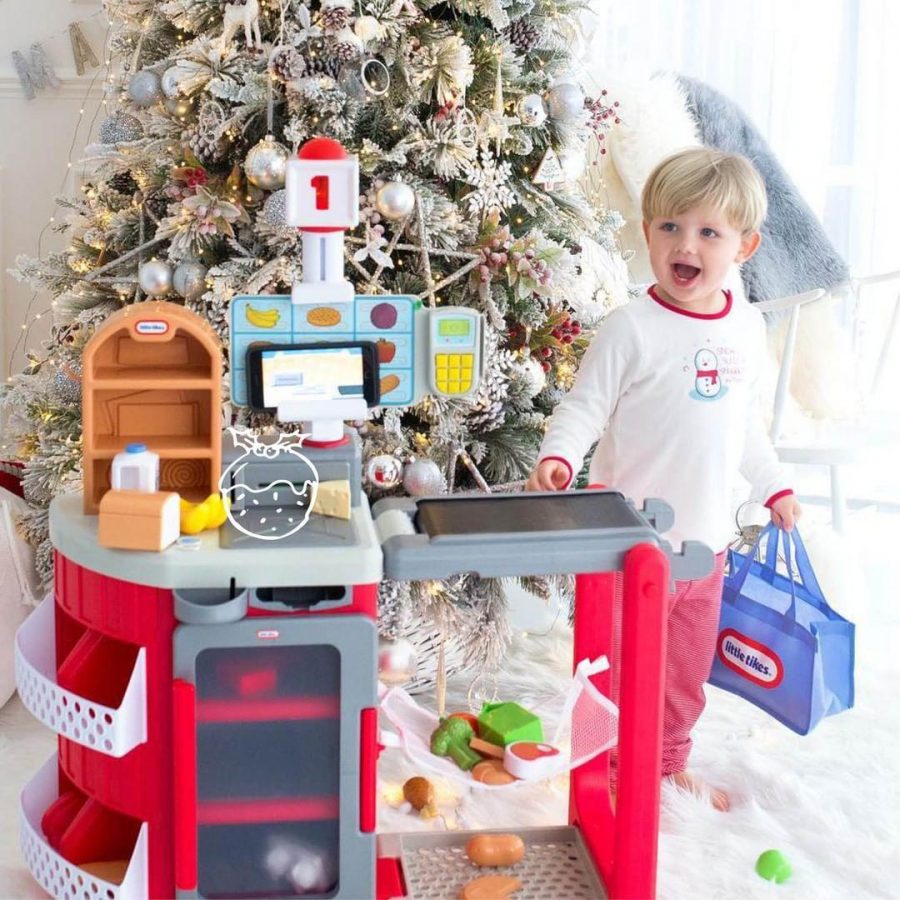 little boy with blonde hair playing with a Little Tikes toy kitchen in front of a christmas tree