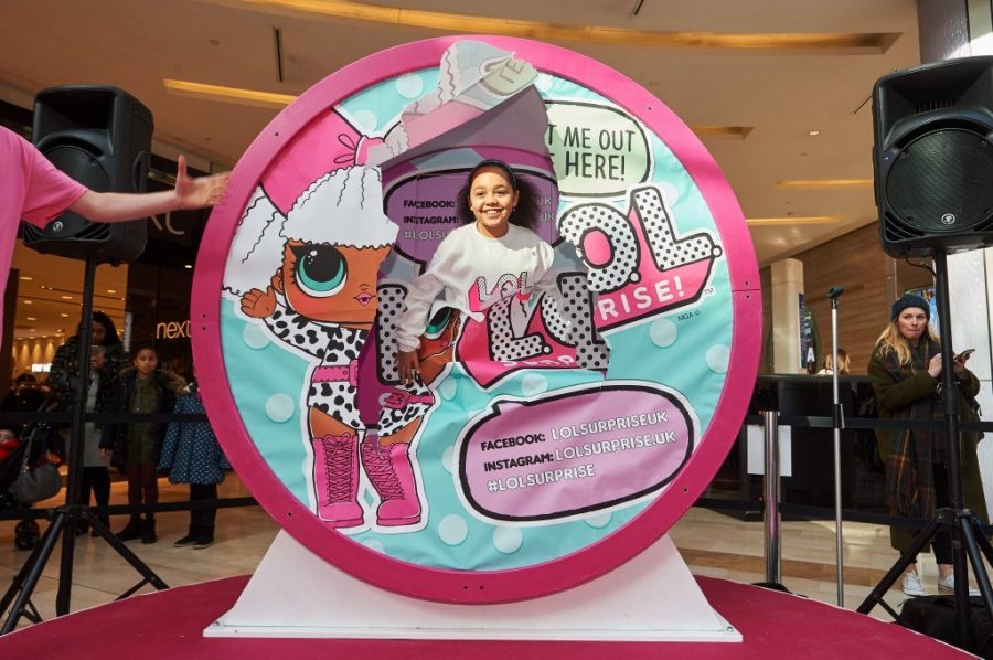 tiana toys and me bursting out of a giant LOL surprise toy ball wearing a white sweatshirt with the pink and white spotty LOL surprise logo