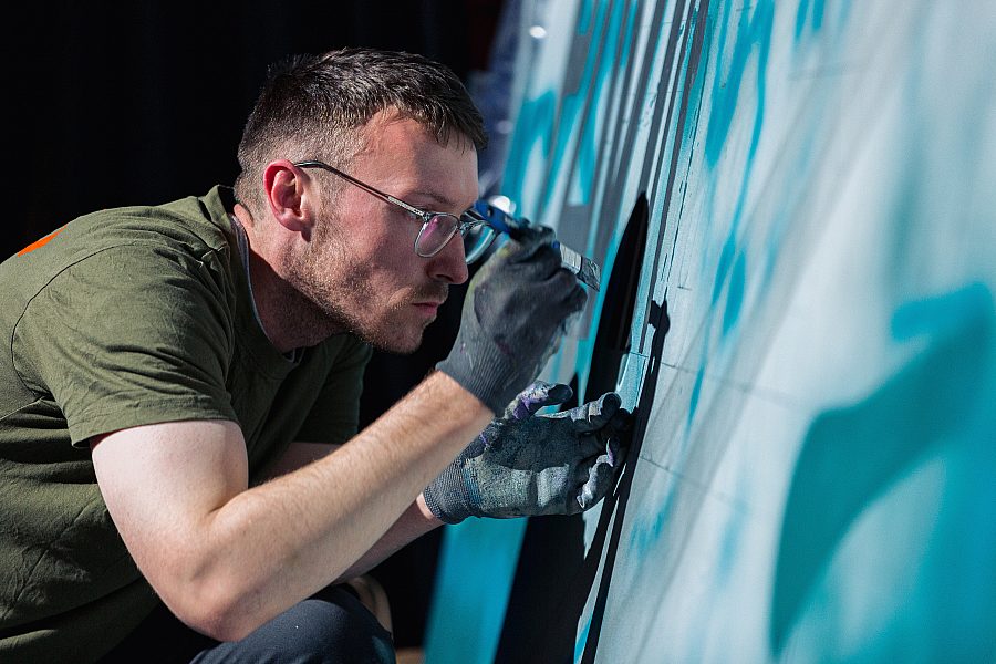 artist Jameson Rogam painting a large blue mural