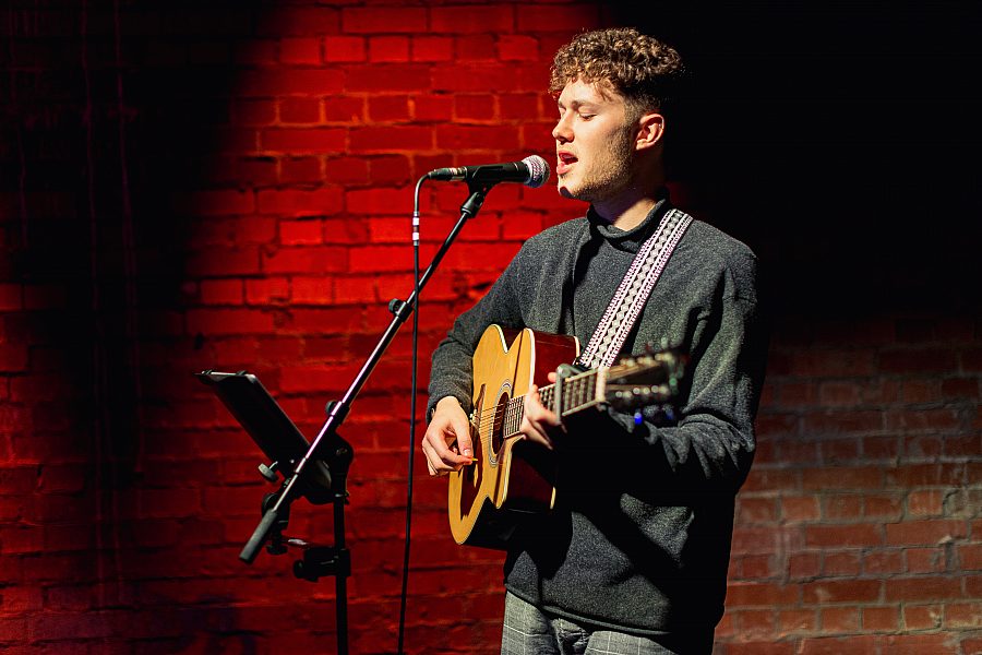Tom Besley from Leeds College of Art singing on stage with a guitar