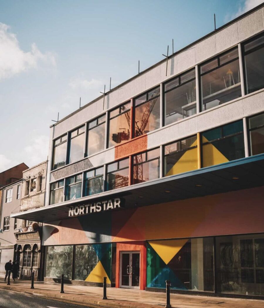 A white Northstar building in Manchester's Northern Quarter with yellow, orange, pink and blue angular shapes painted onto the outside, plus a black sign with Northstar in white capitals